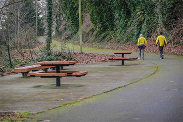 A couple of walkers in yellow jackets enjoy a rainy walk on the Interurban Trail