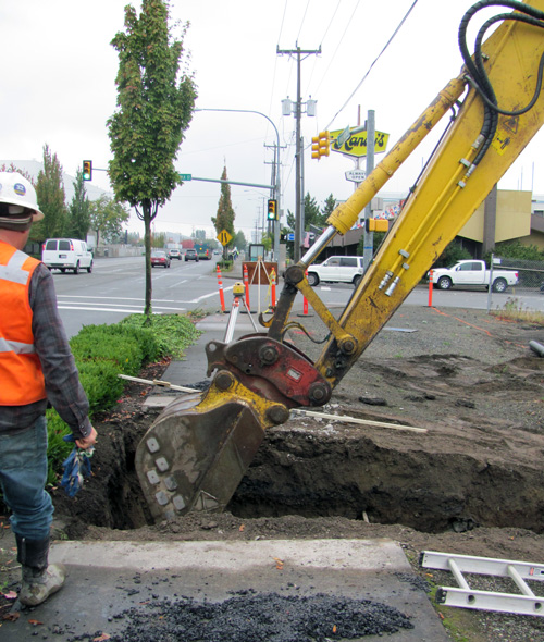Worker observing a back how excavate a trench for a sewer extension.