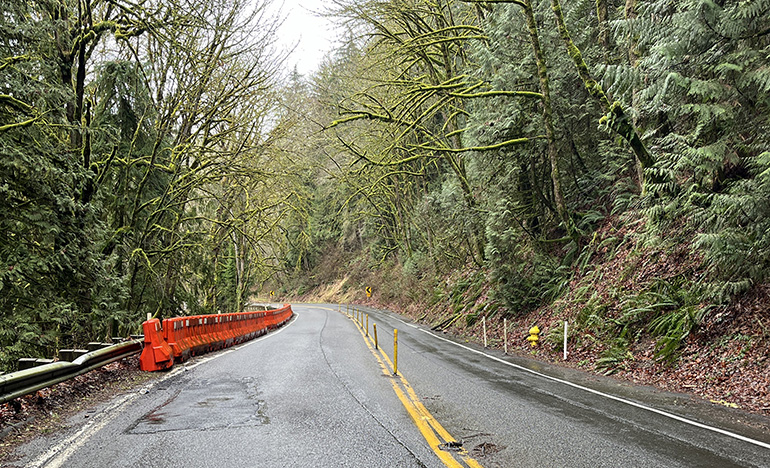 An orange barrier next to the damaged section of wall and narrowed the travel lanes.