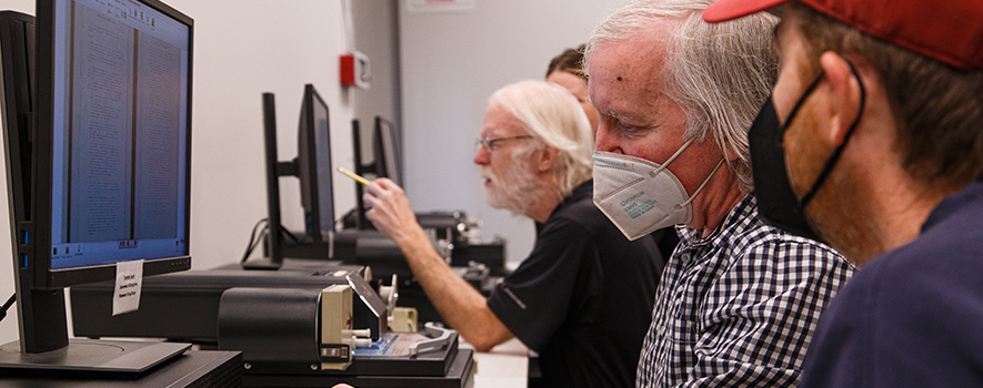 Several people sitting a computer station looking at a monitor